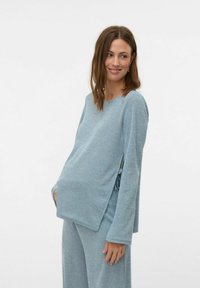 Maglione maternità blu chiaro con maniche lunghe, soffice al tatto, e lacci laterali, abbinato a pantaloni coordinati di colore e texture simile.