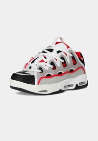 Zapatilla deportiva para hombre en blanco, negro, rojo y gris, con distintivas superposiciones laterales onduladas, suela gruesa y amortiguación de aire visible.
