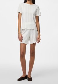 Lätt, strukturerad tvådelad set i off-white; kortärmad topp med volangkant, matchande shorts. Mjuk, ventilerande tyg.
