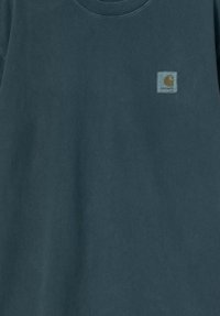 T-shirt en coton bleu marine avec un col rond et des manches courtes. Présente une petite étiquette rectangulaire avec le logo Carhartt sur le côté gauche de la poitrine.