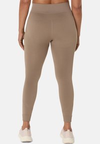 Beige high-waisted leggings made of stretchy material with seamless design, tapered ankles, and minimal hardware, paired with light sneakers.
