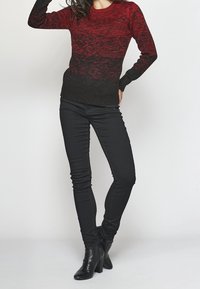 Roter und schwarzer gestrickter Pullover mit einem Farbverlaufsmuster, kombiniert mit schwarzen Skinny Jeans und Knöchelstiefeln. Gerippte Bündchen und Saumdetails.