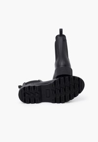 Botas de tobillo de goma negra con suelas texturizadas, que cuentan con una cinta de agarre y un acabado liso, diseñadas para la durabilidad y la comodidad.