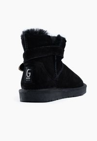 Botas de tobillo de ante negro con forro de piel sintética, suela de goma plana y una correa ajustable de Velcro con una etiqueta de logo en el talón.