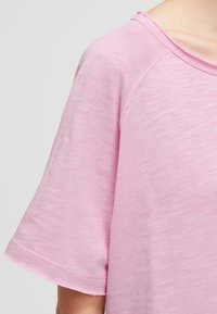 Close-up of a person wearing a light pink, short-sleeved shirt with visible stitching on the sleeve and neckline.