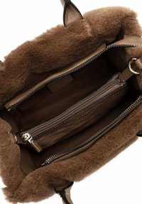 Sac à main marron avec doublure en fausse fourrure, intérieur beige, plusieurs compartiments et zips. Extérieur texturé avec accents en cuir.