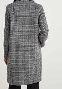 Pitkä ruudullinen takki, jossa on musta, valkoinen ja harmaa väri, rakenteellinen kaulus ja pitkät hihat, valmistettu teksturoidusta kankaasta.