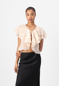 Haut en chiffon de couleur pêche avec des volants superposés et une fermeture à nouer à l'avant. Porté sur une jupe en satin noire. Texture lisse et design doux.
