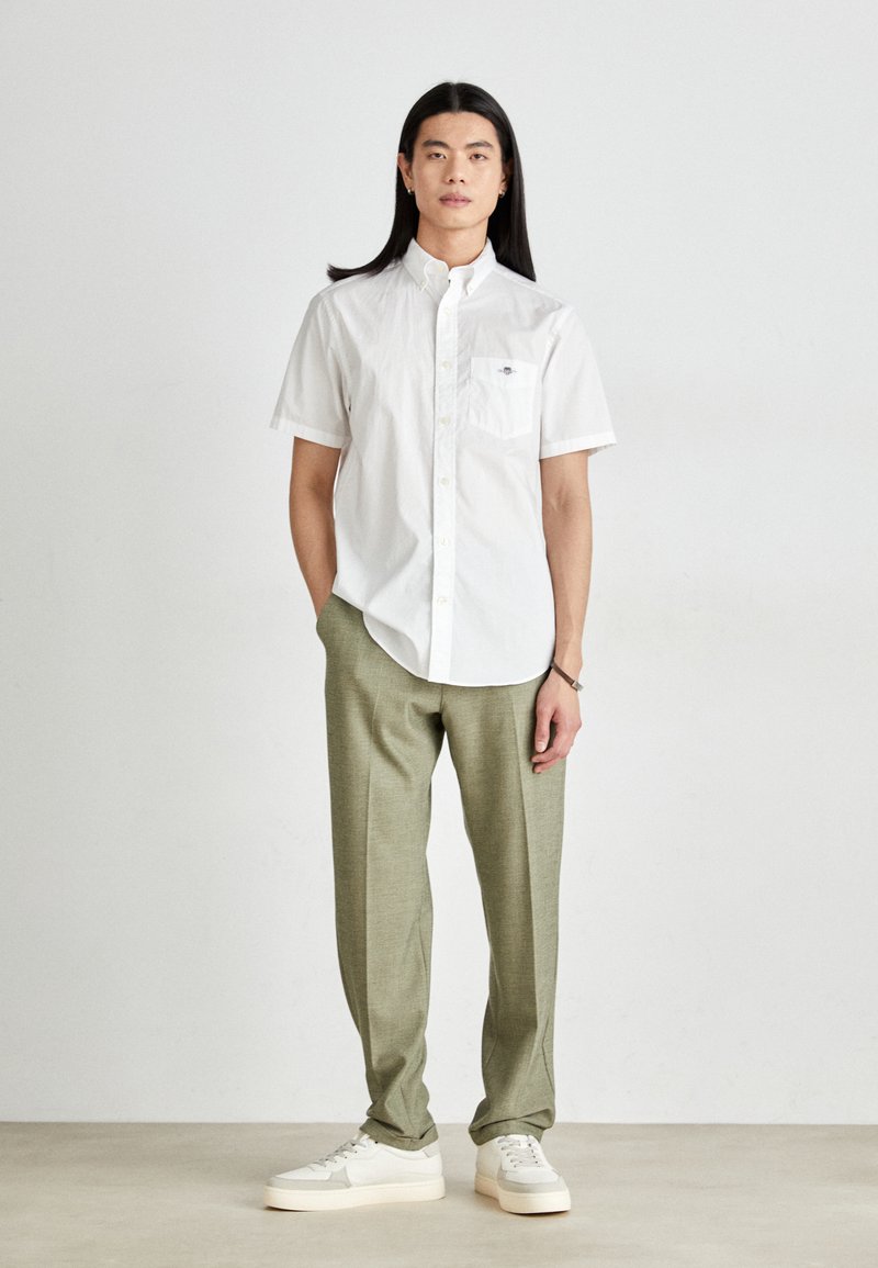 Chemise blanche à manches courtes avec un col boutonné et une poche poitrine, associée à un pantalon vert clair et des baskets blanches. Ajustement simple et tailleur.