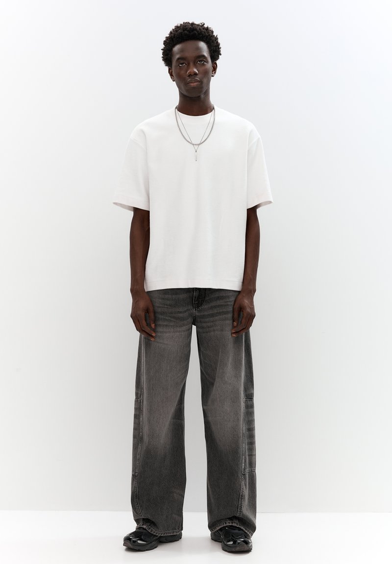 White oversized cotton t-shirt and gray wide-leg jeans. Features a smooth texture and structured fit. Black sneakers and layered silver necklaces.