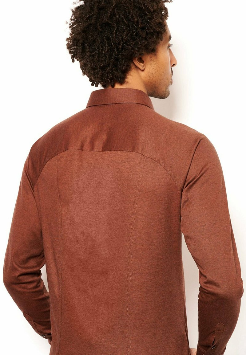 Bruine blouse met lange mouwen en een gladde textuur, voorzien van een contrasterende donkere yoke en subtiele stiksels aan de achterkant.