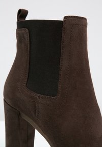 Bottine en daim marron avec panneau latéral élastique noir et languette, dotée d'un talon haut et épais.