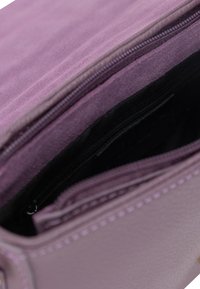 Interno di una borsa in pelle viola che mostra una morbida texture scamosciata con una tasca con zip nera e un rivestimento liscio, caratterizzato da dettagli di cucitura visibili.