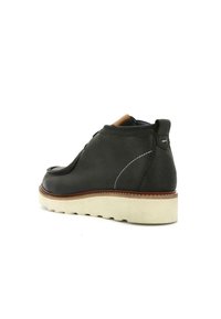 Scarpa alla caviglia in pelle nera con design curvato, suola in gomma e intersuola beige a contrasto. Presenta cuciture decorative bianche e tallone rinforzato.