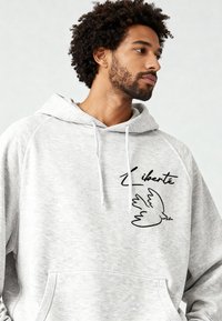 Felpa grigia con cappuccio con tasca frontale, caratterizzata da testo ricamato nero "Liberté" e grafica di una colomba. Tessuto morbido e strutturato, cappuccio con coulisse.