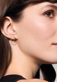 Złota kolczyk w kształcie kółka z młotkowanym wykończeniem, z małym otworem. Noszony na uchu, prezentujący błyszczące wykończenie i elegancki design.