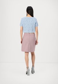 Top corto azul claro con estampado floral, combinado con una falda rosa texturada a la altura de la rodilla y sandalias de tacón cuadrado gris.