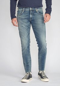 Blauwe denim jeans met een vervaagd ontwerp, voorzien van vijf zakken, een knoopsluiting en een slim fit, gecombineerd met zwarte high-top sneakers.
