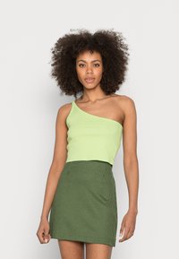 Top cropped verde-claro com uma só alça, combinado com uma saia mini padrão houndstooth verde e preto. Textura suave, design ajustado.