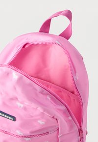 Ροζ σακίδιο πλάτης με μικρά λευκά σχέδια ελαφιών, μπροστινή τσέπη με φερμουάρ μερικώς ανοιχτή και υφασμάτινη λαβή βρόχου πάνω σε λευκό φόντο.