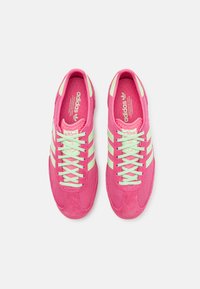 Ljust rosa sportskor med nät- och mockamaterial, med neongröna accenter, tre ränder och platta snören.