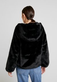 Zwarte nepbonten hoodie met een ruime pasvorm, capuchon en brede mouwen. Zachte textuur, gedragen met blauwe jeans, zichtbaar vanaf de achterkant.