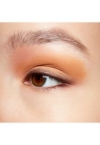 Close-up van een oog met een gemengd warme oranje oogschaduw, met een soepele textuur en een natuurlijke wenkbrauw. De iris is bruin en heeft duidelijke wimpers.