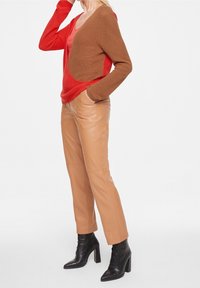 Cardigan en tricot avec un design en blocs de couleurs marron et rouge, associé à un pantalon beige brillant et des bottes à talons noires. Texture lisse dans l'ensemble.