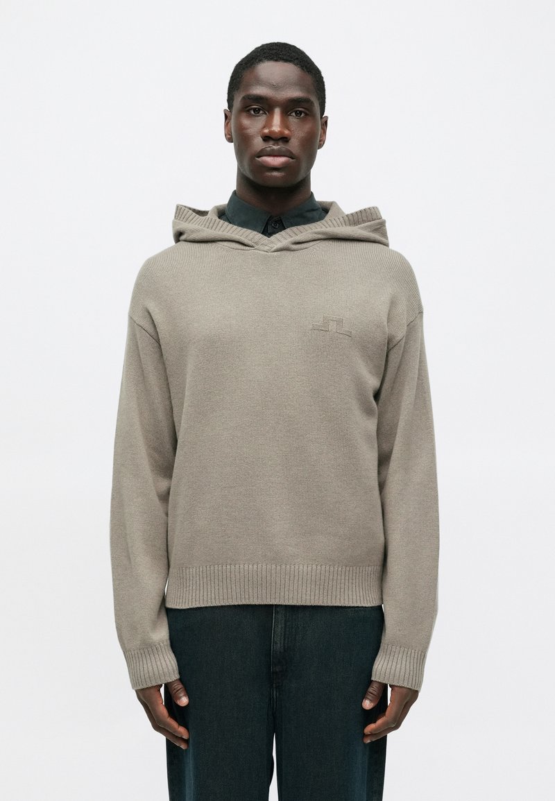 Ανοιχτό καφέ πλεκτή κουκούλα με ριμπ τελειώματα �και μανίκια. Διαθέτει σχέδιο σε σχήμα V και μια διακριτική λεπτομέρεια λογότυπου στο στήθος. Συνδυάζεται με σκούρα τζιν.