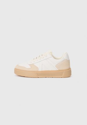 Baskets basses blanches avec des accents en daim beige, lacets blancs et semelle en caoutchouc beige épaisse, montrées de profil sur un fond uni.