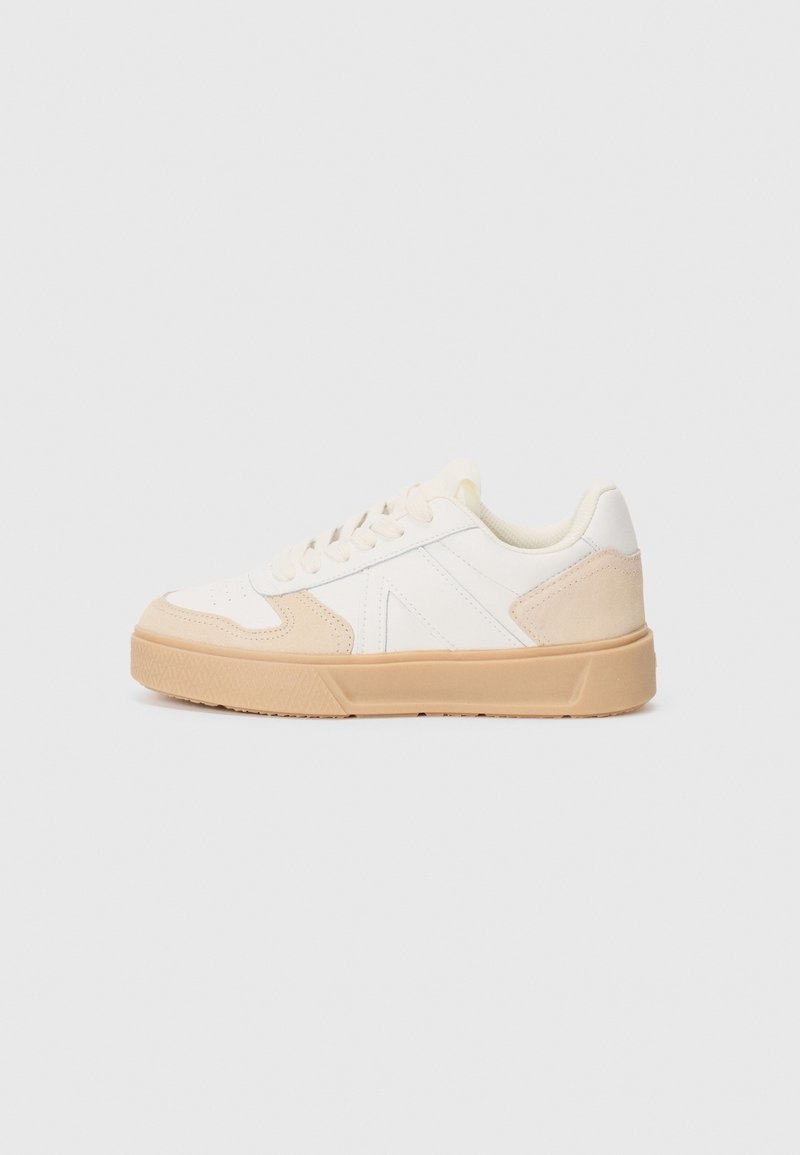 Baskets basses blanches avec des accents en daim beige, lacets blancs et semelle en caoutchouc beige épaisse, montrées de profil sur un fond uni.