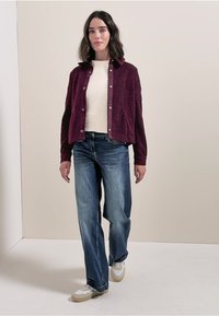 Burgundowa krótka kurtka z teksturowanej tkaniny, zapinana na guziki, w połączeniu z jasnoniebieskimi spodniami o szerokich nogawkach i białymi trampkami.