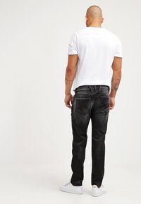 Vaqueros de mezclilla negra con un corte ajustado, que cuentan con un diseño de cinco bolsillos y costuras en contraste, combinados con una camiseta blanca básica y zapatillas blancas.