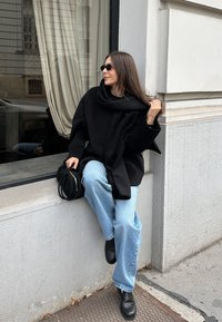 Przesadnie duży czarny wełniany płaszcz z wysokim kołnierzem, w połączeniu z jasnoniebieskimi dżinsami i czarnymi skórzanymi butami. Dodatkowo mała czarna torebka.