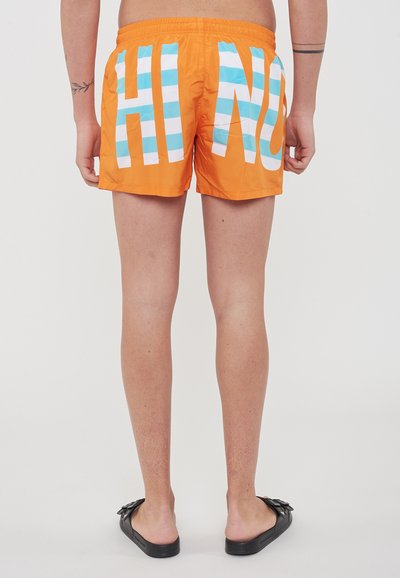 Pantaloni da bagno arancioni con scritte a righe bianche e blu "HIN" sul retro, caratterizzati da una vita elastica e un tessuto liscio e leggero.