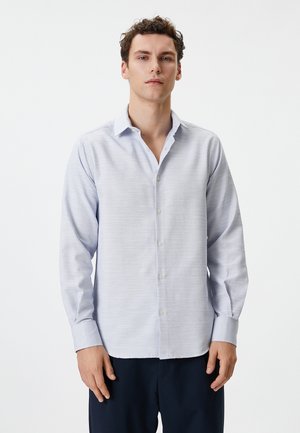 Camisa de botón de manga larga en azul claro, con un sutil patrón texturizado, cuello plano y puños de un solo botón; fabricada con un tejido suave.