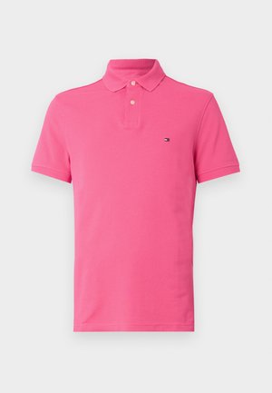 Różowa koszulka polo wykonana z bawełny, z dwa guziki przy dekolcie, krótkimi rękawami i małym logo na lewej piersi. Gładka tekstura.