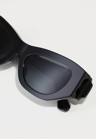 Óculos de sol oversized pretos com um acabamento brilhante, lentes escuras e um design angular com um destaque distintivo na lateral.