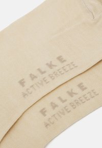 Bež čarape izrađene od teksturiranog materijala, s utisnutim brendom "FALKE ACTIVE BREEZE" u svjetlijoj nijansi.