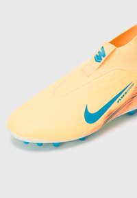 Fotbalová kopačka Nike v jasně žluté barvě s texturovaným svrškem, modrými akcenty, aerodynamickým tvarem a podrážkou s kolíky pro lepší trakci.
