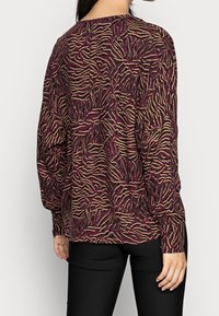 Langärmliges Shirt in Burgunderrot mit einem strukturierten Muster aus wellenförmigen goldenen und schwarzen Linien; lockere Passform mit Rundhalsausschnitt und gerippten Bündchen.