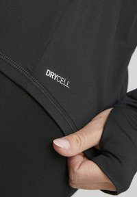 Top atlético negro con un diseño ajustado, textura suave y un logo "DRYCELL" visible. Aberturas para los pulgares en las mangas para mayor comodidad.