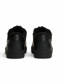 Sneakers in pelle nera con fodera nera pelosa, caratterizzati da un tallone posteriore testurizzato e il marchio "TOMMY HILFIGER" in rilievo sulla suola.