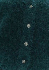 Tummanpetroolinvihreä, pehmeästä kankaasta valmistettu neuletakki, jossa on viisi hopeanväristä ruusunmuotoista nappia ja pehmeä pinta. Sopii kerrospukeutumiseen tai casual-tyyliin.