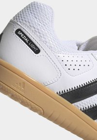 Chaussure de sport blanche avec tige en mesh, design perforé, accents noirs et semelle en caoutchouc beige. L'étiquette indique "SPEZIAL LIGHT."