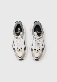 Lacoste sneakers featuring a white mesh upper, metallic gold and silver accents, black detailing, and white laces. Rounded toe and cushioned sole.