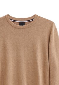 Maglione beige lavorato a maglia con colletto rotondo e polsini a coste. Presenta un dettaglio logo discreto sul petto. Tessuto morbido con una consistenza liscia.
