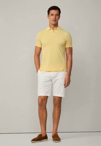 Vaaleankeltainen poolopaita yhdistettynä valkoisiin shortseihin. Mukava istuvuus, lyhyet hihat ja tasainen kaulus. Ruskeat loafersit täydentävät asun.