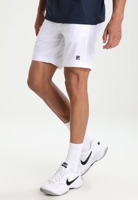 Witte sportshorts gemaakt van een lichtgewicht materiaal, met een klein zwart logo. Gecombineerd met witte sneakers en sokken.