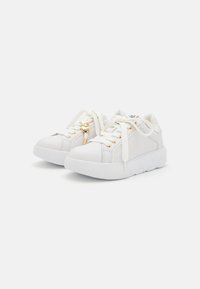Fehér sneaker, sima bőrből készült, aranyszínű fémrészletekkel, lapos fűzőkkel és texturált gumitalppal. Kerek orrész és minimális varrási részletek jellemzik.